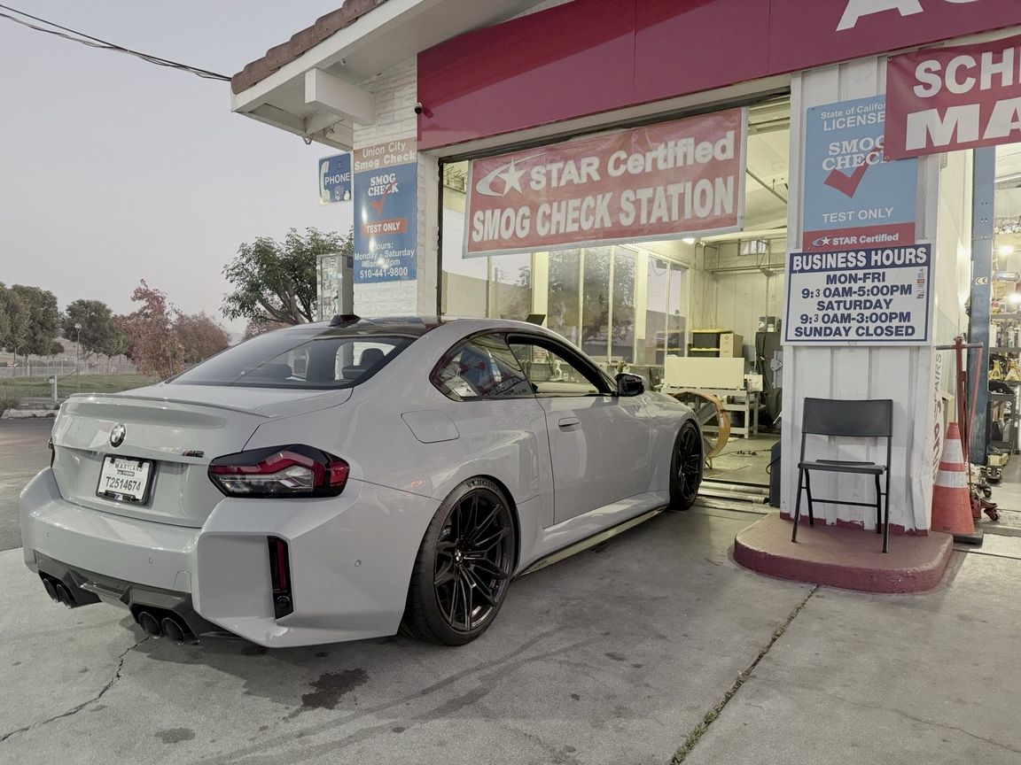 Gray BMW M2 at the Union City Smog Check bay, with the STAR Certified banner and business hours sign